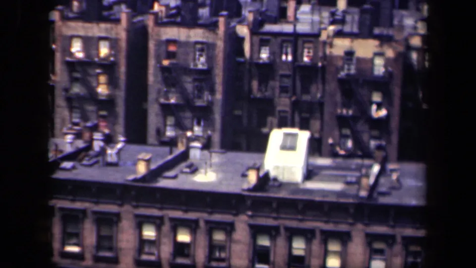 1941 New York overhead frame with brick apartment blocks, exterior fire escapes, vents, chimneys and a pale rooftop structure.