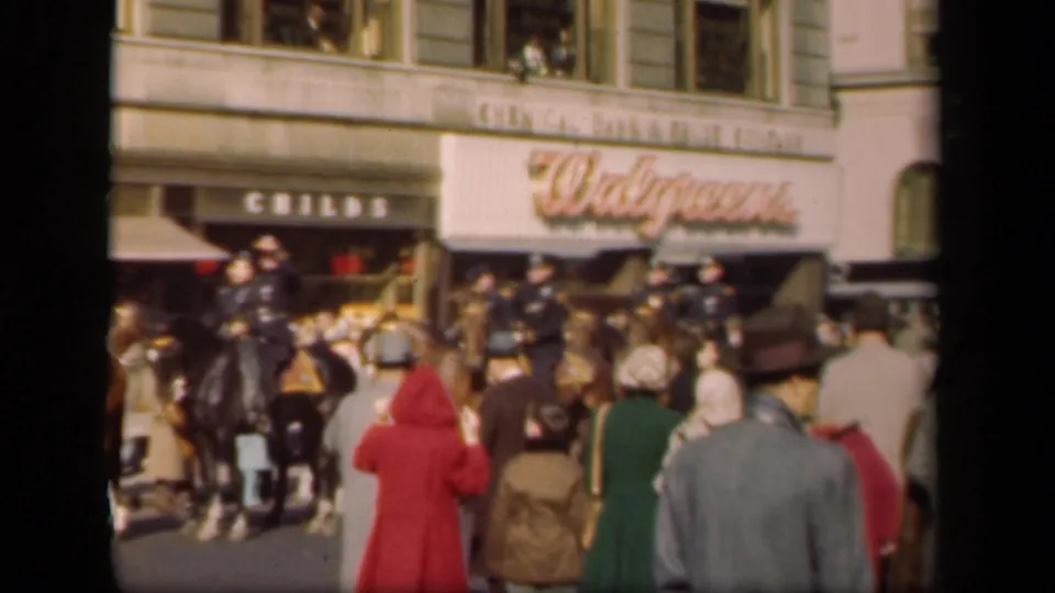 1941 New York street crowd passing Childs and Walgreens storefronts, with mounted police on horseback among pedestrians.