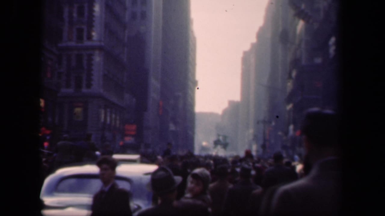Crowded avenue with older cars, pedestrians, and tall buildings in haze.