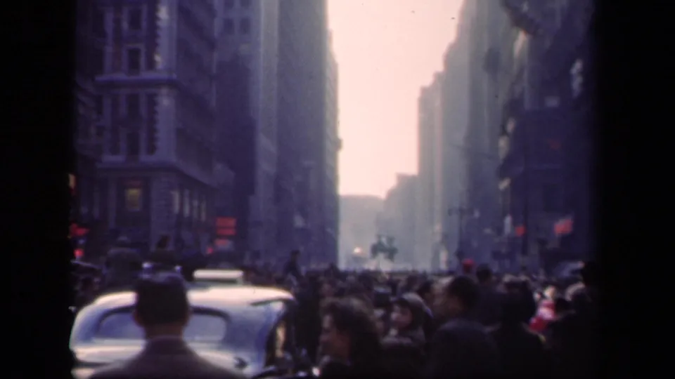 Crowded 1941 New York street view with pedestrians, older cars, tall buildings, and a mounted figure visible down the avenue.