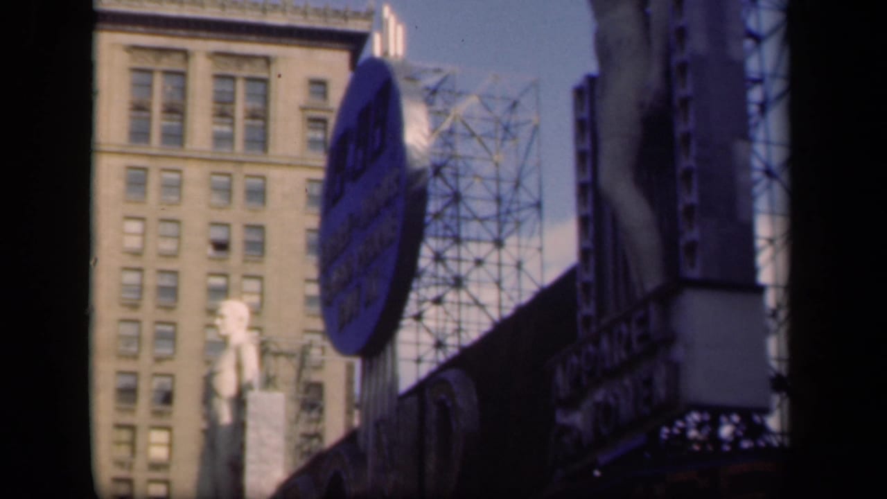 1941 New York street view with a blue circular billboard, metal framework, a mannequin-like sidewalk figure, and a tall windowed building behind.