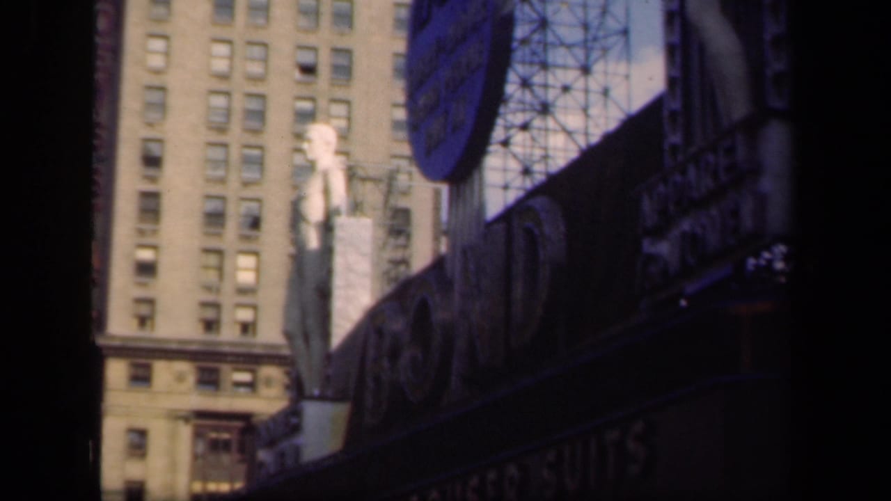 1941 New York street view with a tall building, dark marquee signage, circular sign, and a pale statue figure above the storefront.