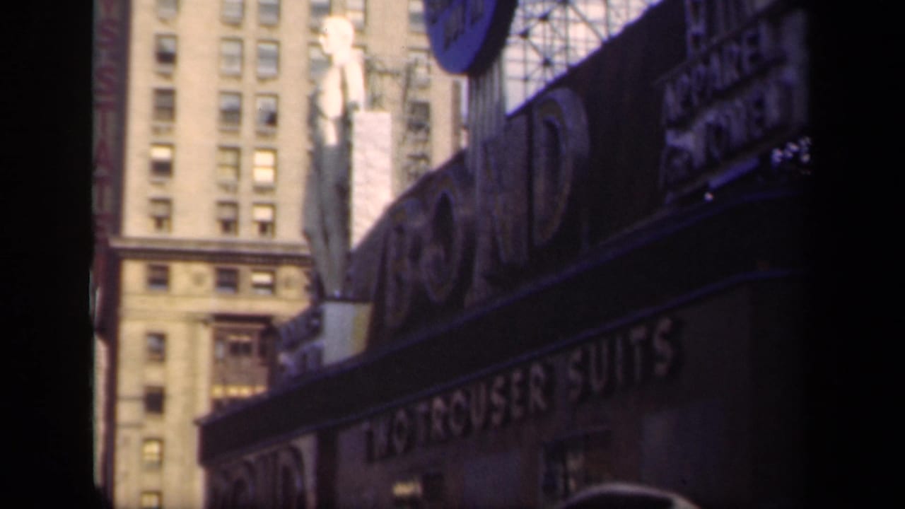 1941 New York commercial block showing large signage, a statue-like figure above the storefront, and a tall windowed building behind it.