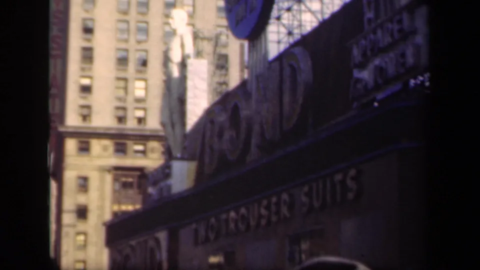 1941 New York commercial block showing large signage, a statue-like figure above the storefront, and a tall windowed building behind it.