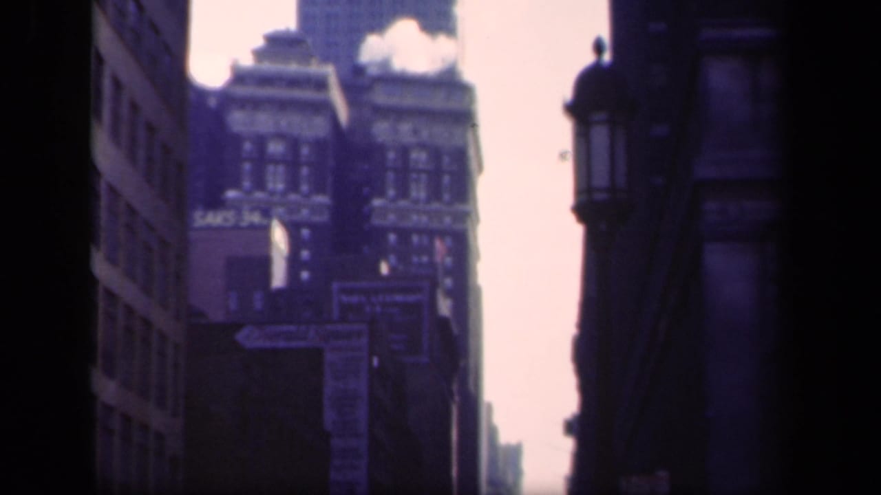 1941 New York frame with a distant skyscraper rising beyond older commercial buildings and visible Saks signage.