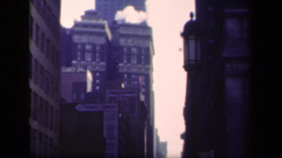 1941 New York frame with a distant skyscraper rising beyond older commercial buildings and visible Saks signage.