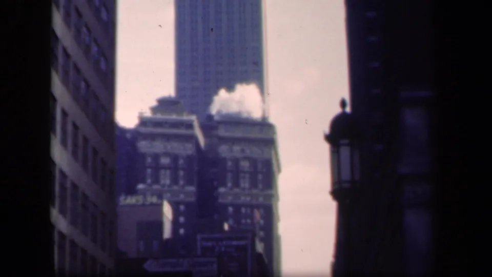 1941 New York upward street view with rooftop steam or smoke, a distant tower, and dark building edges framing the scene.