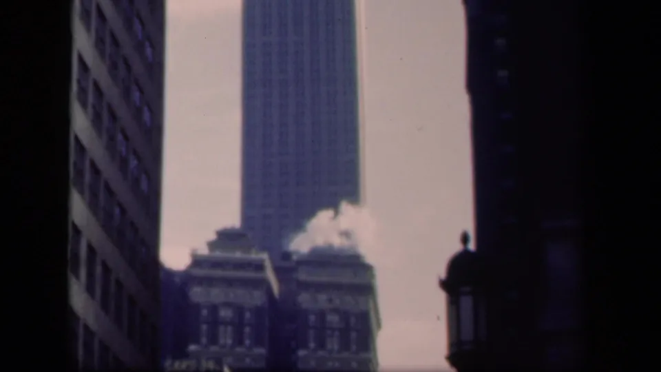 1941 New York view centering a tall skyscraper between shadowed facades, with rooftop steam and commercial signage below.