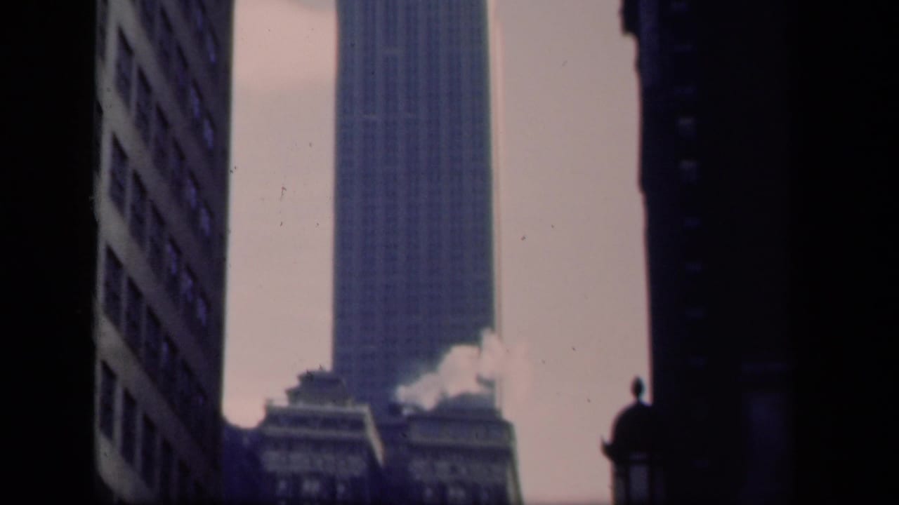 1941 New York home-movie frame showing the Empire State Building rising between shadowed high-rise facades.