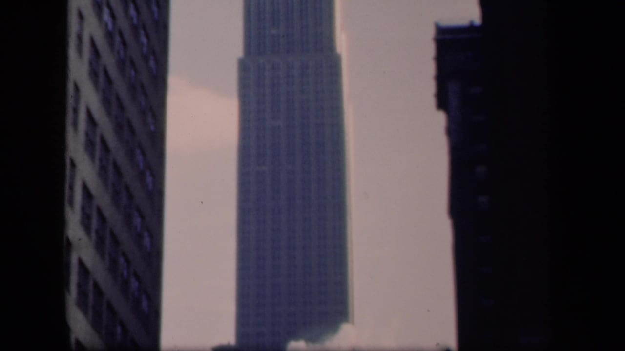 Upper portion of the Empire State Building seen between tall dark buildings.