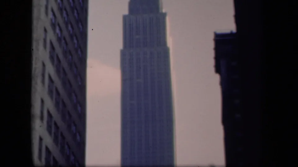 1941 New York home-movie frame showing the Empire State Building during an upward pan through a Manhattan street canyon.