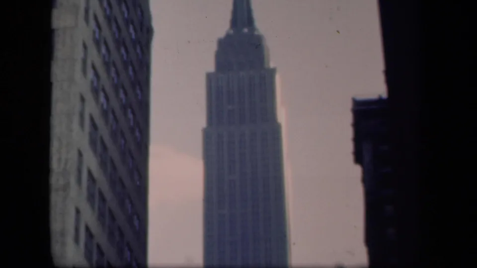 1941 New York frame with the Empire State Building spire visible against a hazy sky, flanked by darker towers.