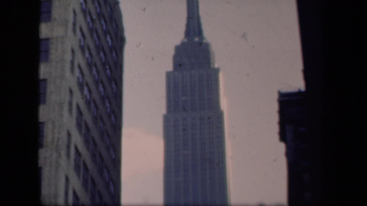 1941 New York home-movie view of the Empire State Building framed by nearby high-rise facades and dark vertical edges.