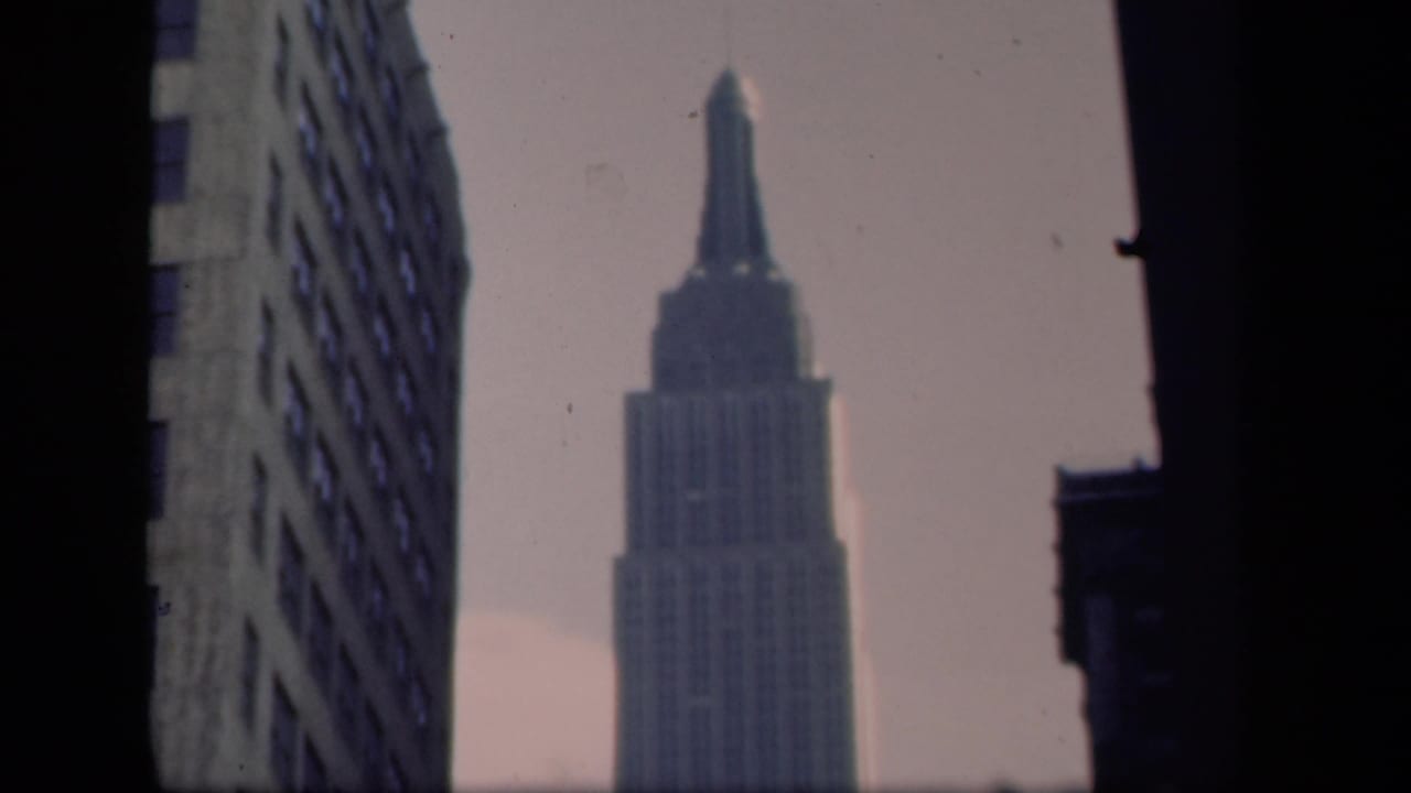 Soft 8mm view of the Empire State Building in New York, held between neighboring buildings under a pale sky.
