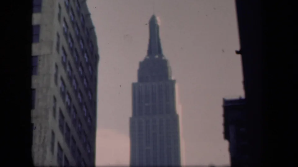 Soft 8mm view of the Empire State Building in New York, held between neighboring buildings under a pale sky.