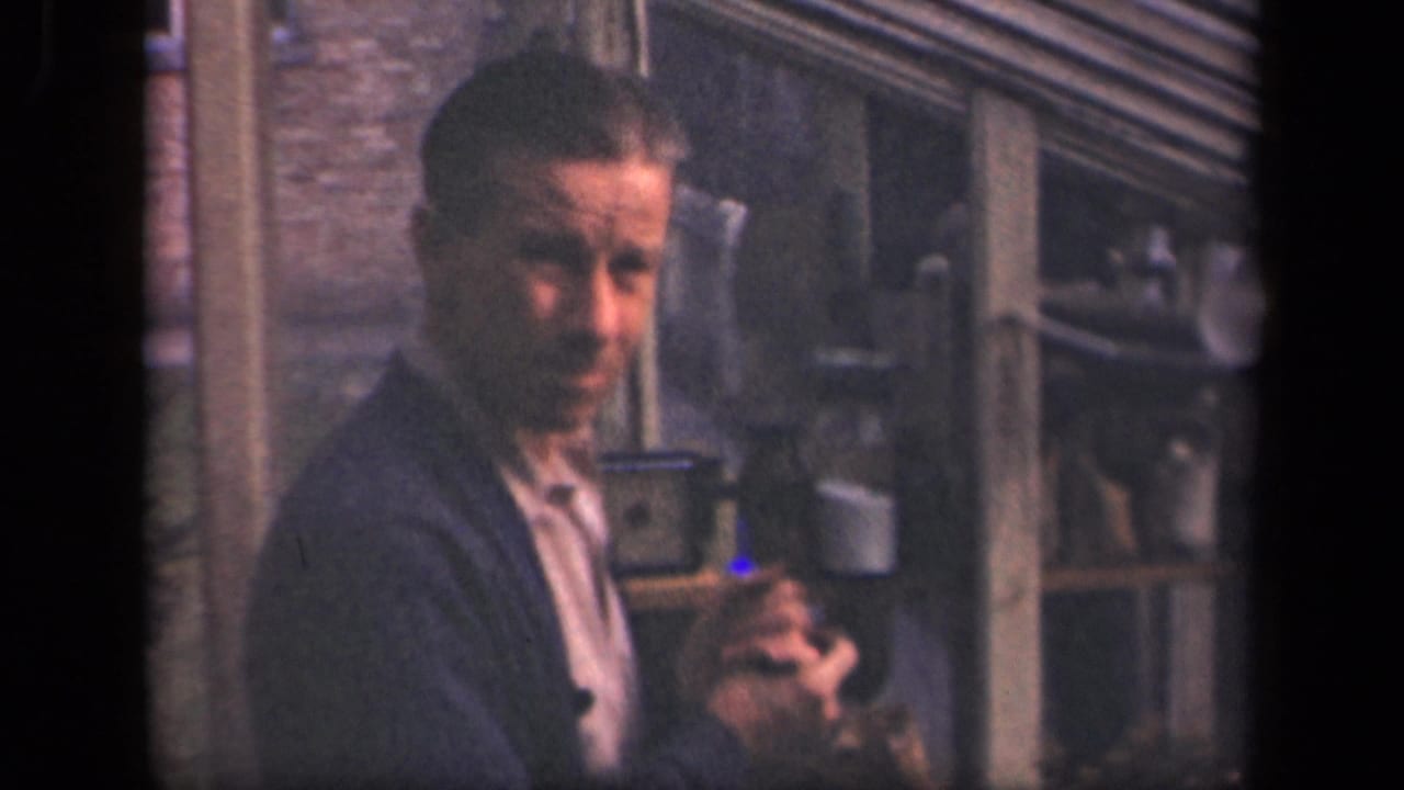Man faces the camera while holding a small object near shelves and glassware.