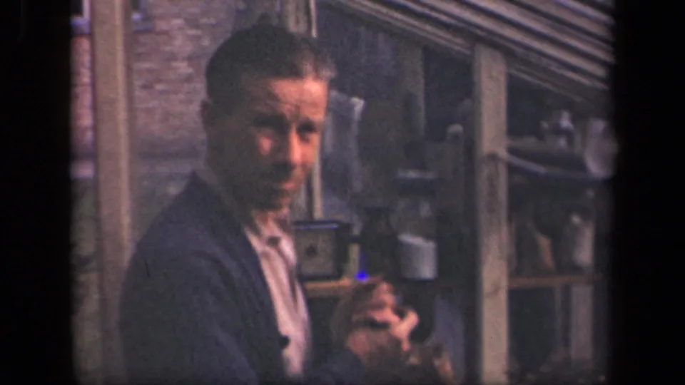 The adult man briefly faces the camera while handling a small item in a 1941 New York lab-like interior.