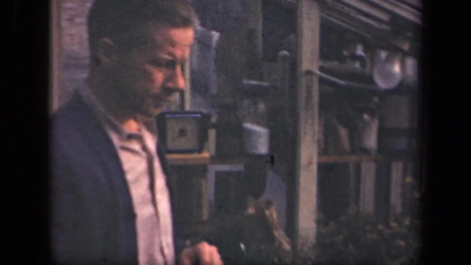 An adult man in a jacket stands near shrubs outside a windowed structure in 1941 New York home-movie footage.