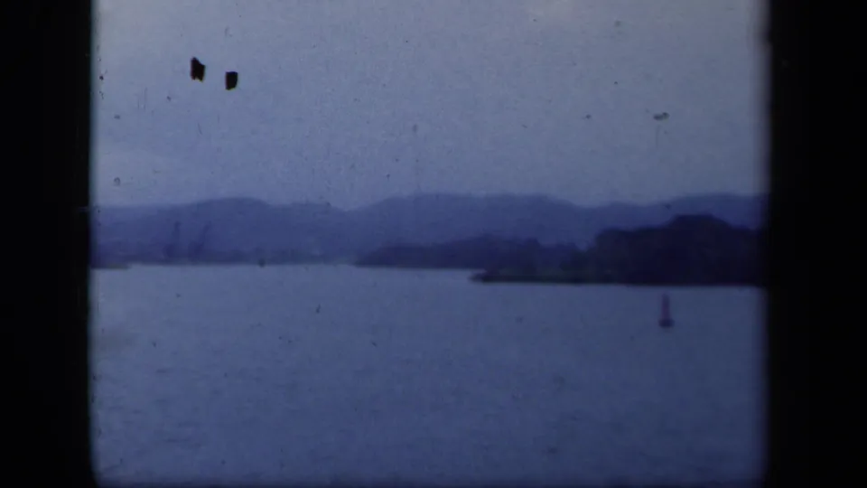 1941 New York 8mm frame of a lake beneath distant mountain ridges, with a shoreline mass and small buoy visible.