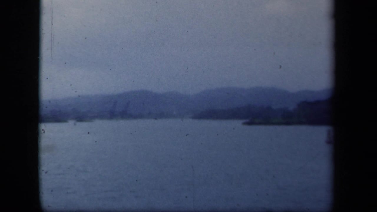 Lake water with hazy mountain ridges and a distant shoreline under an overcast sky.