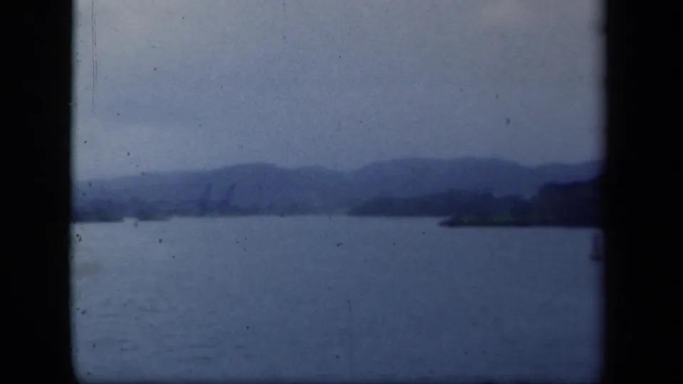 1941 8mm home-movie frame of a lake in New York, with soft mountain silhouettes, distant shore, and blue-tinted film grain.