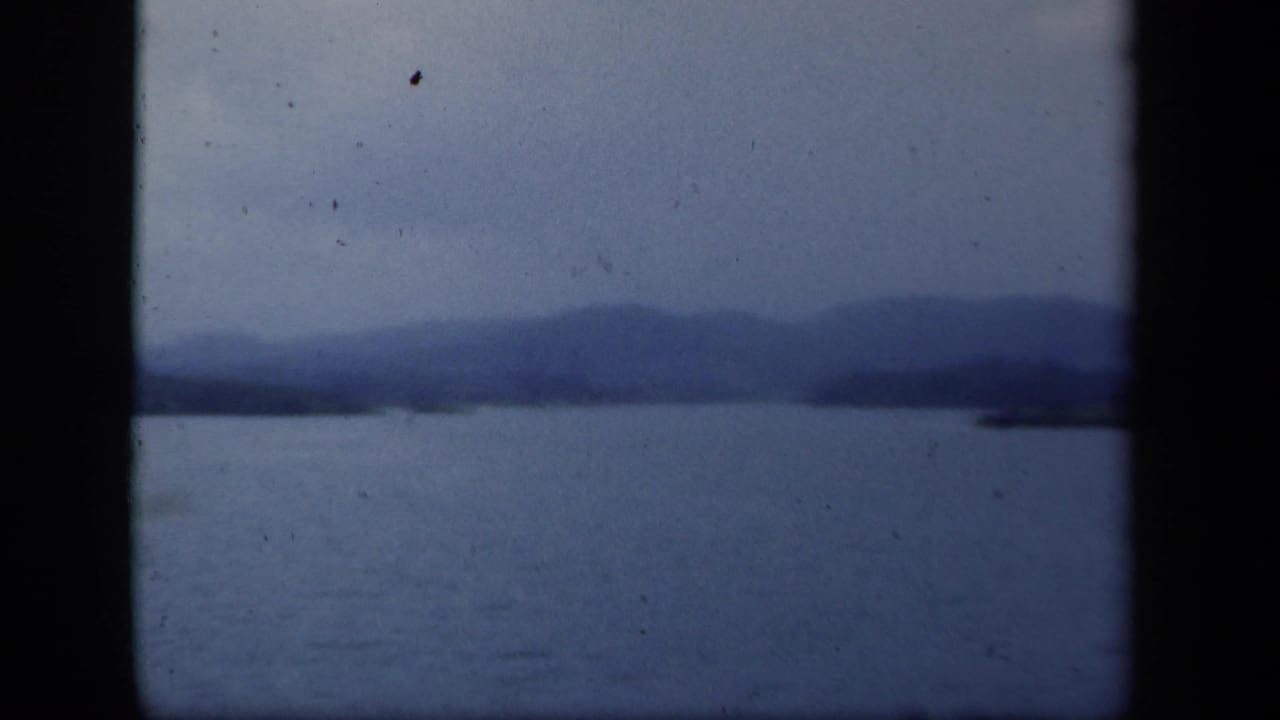 Blue-tinted 8mm frame showing open lake water, hazy mountain backdrop, and a faint shoreline, consistent with the New York metadata.