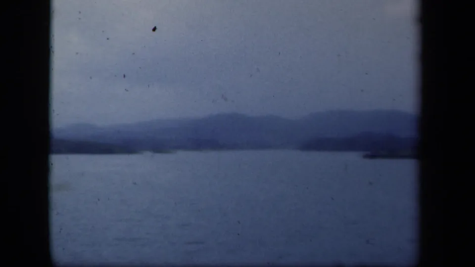 Blue-tinted 8mm frame showing open lake water, hazy mountain backdrop, and a faint shoreline, consistent with the New York metadata.