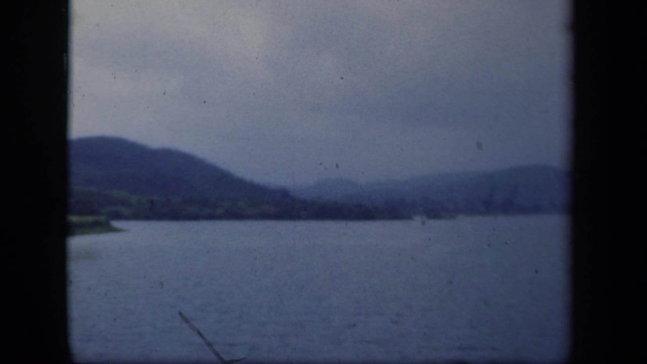 Wide waterway with distant hills under an overcast sky, framed by dark 8mm gate edges.