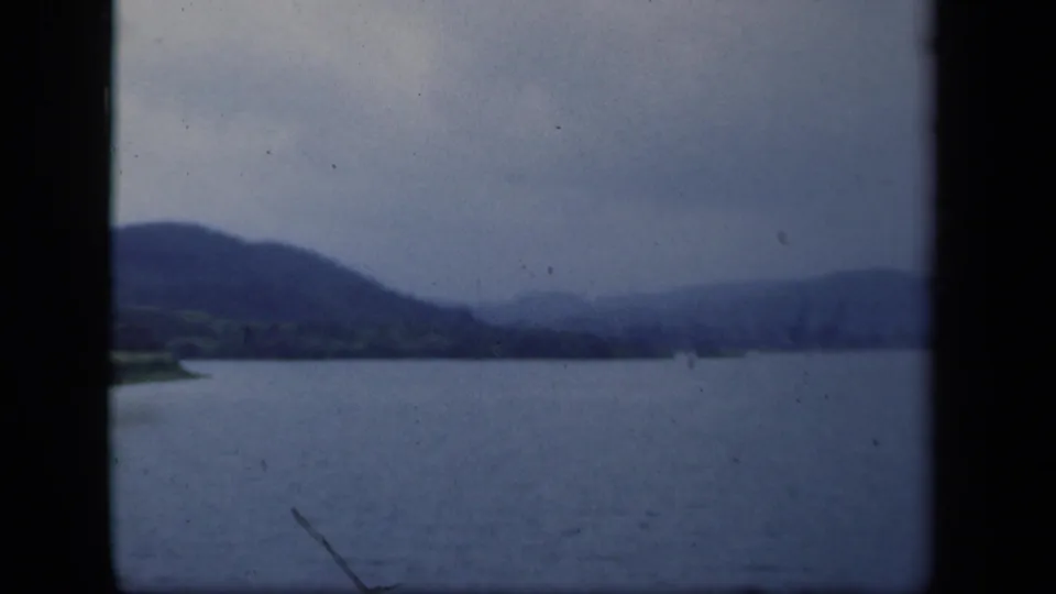 1941 New York 8mm frame showing broad water, low shoreline, and hazy mountain ridges under gray sky.