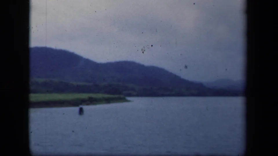1941 New York 8mm frame with green shoreline, broad water, distant hills, and a small buoy in view.