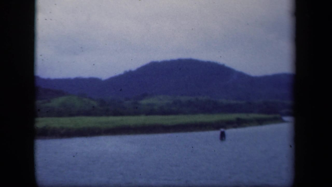 1941 New York 8mm frame with lake water, a small floating marker, green shore, and blue distant hills.