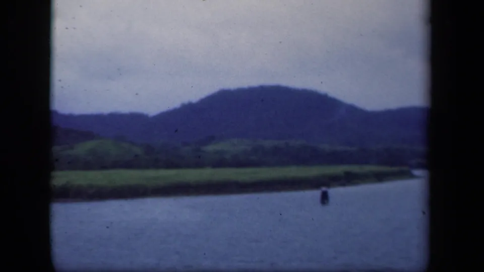 1941 New York 8mm frame with lake water, a small floating marker, green shore, and blue distant hills.