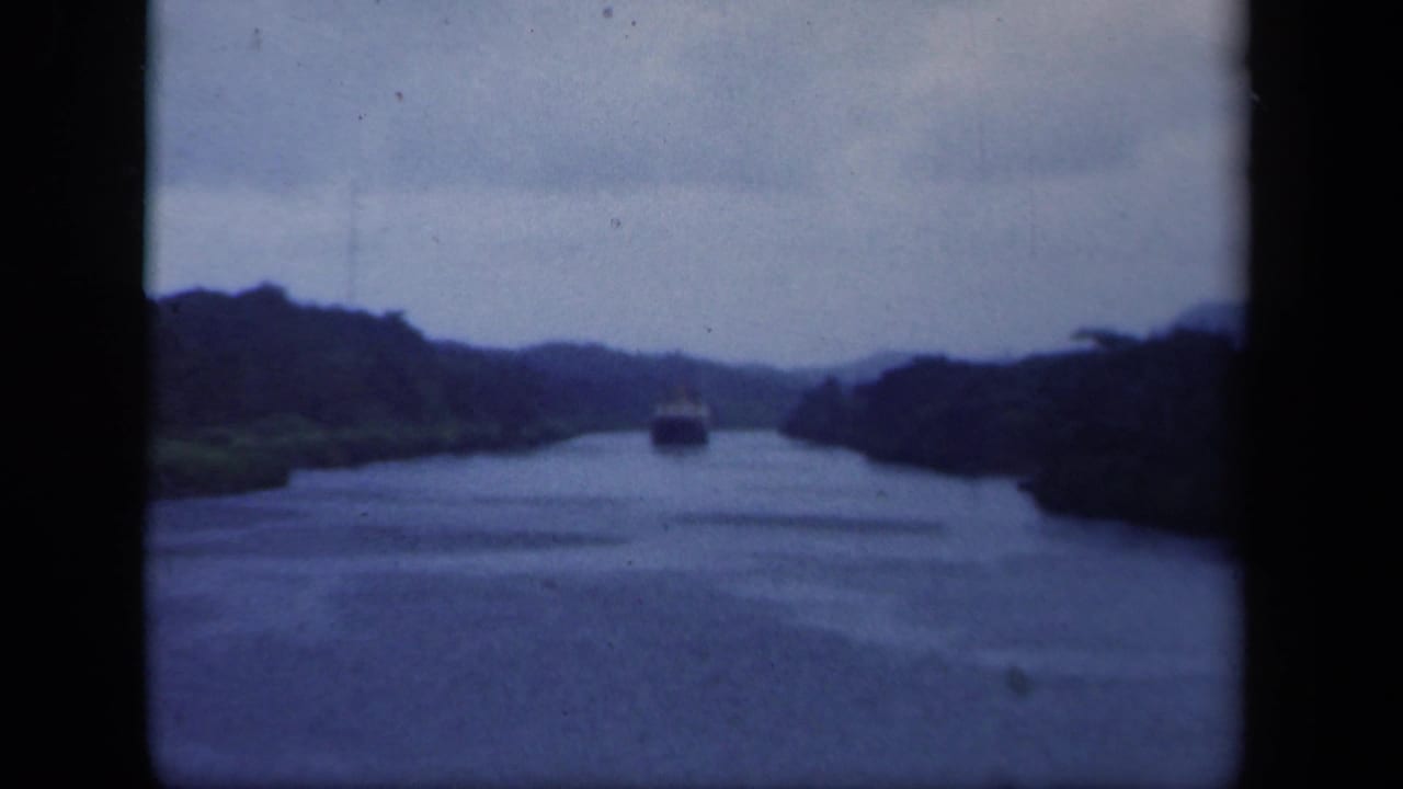 1941 New York home-movie frame with a small vessel approaching along a forest-lined channel in soft blue-gray light.