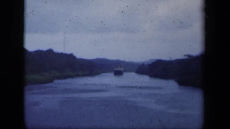 1941 New York 8mm frame showing a ship farther along a calm forested waterway under an overcast sky.