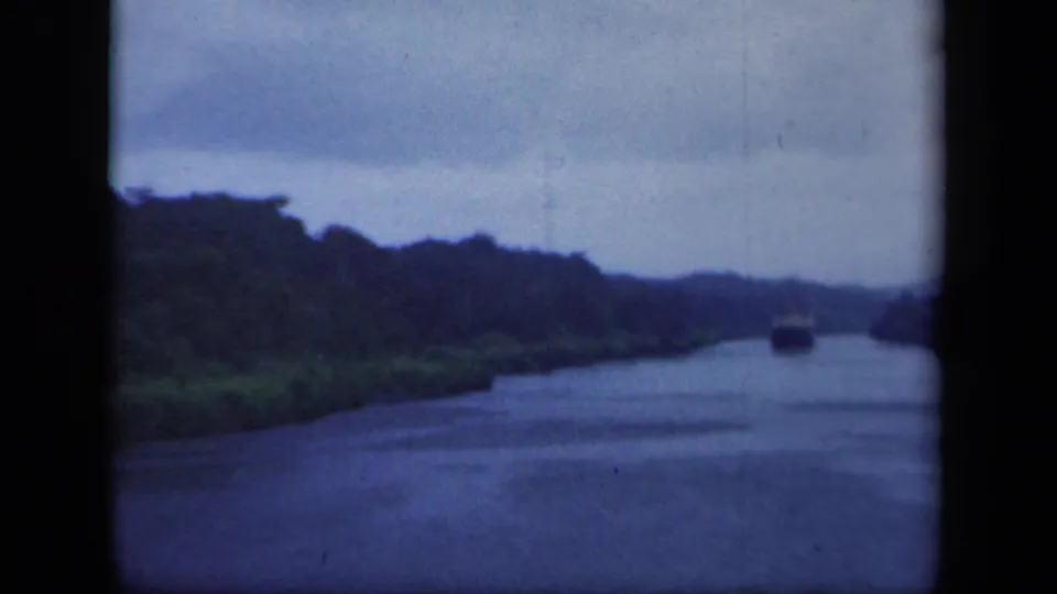 A distant boat moves through a tree-lined New York waterway in 1941 footage, seen across soft blue-toned 8mm film.