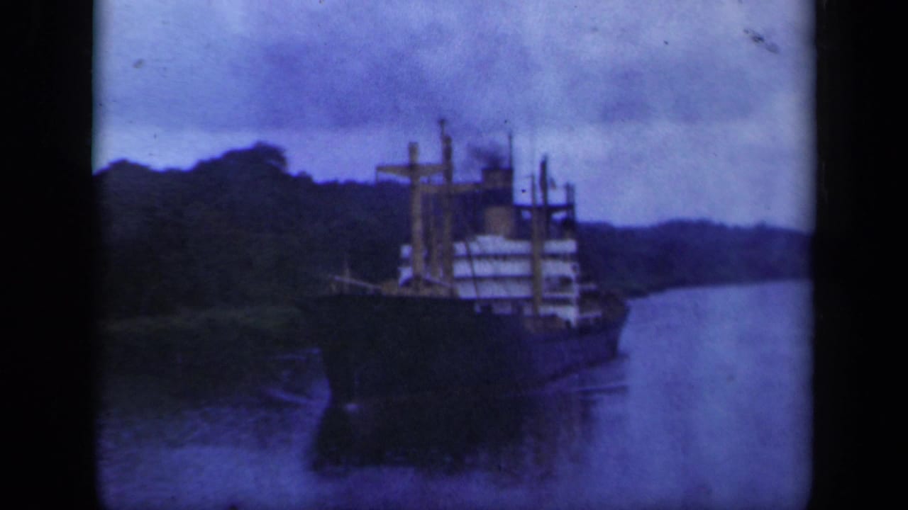 Blue-tinted 8mm view of a cargo ship navigating a calm, narrow waterway bordered by wooded hills in the 1941 New York clip.