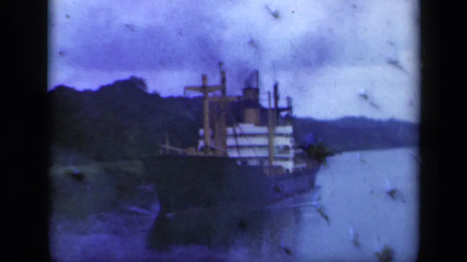 Soft 8mm frame of a cargo ship on a narrow New York waterway, with tree-covered banks and visible dust from the film scan.