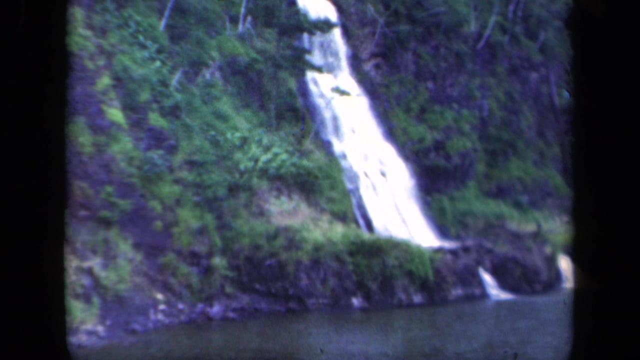 1941 New York 8mm frame showing a bright waterfall on a wooded mountainside above a dark pool, with soft focus and black reel borders.