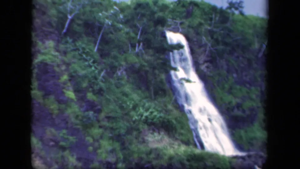 1941 New York home-movie frame with a tall white cascade running through green brush and rock on a steep wooded slope.