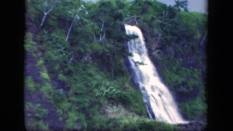 Soft 8mm frame from 1941 New York showing a waterfall descending a forested mountainside with dark rocks and dense greenery.