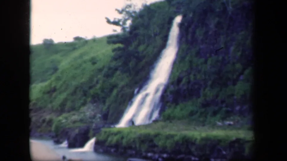 1941 New York 8mm frame showing a waterfall, rocky bank, and surrounding forest greenery.