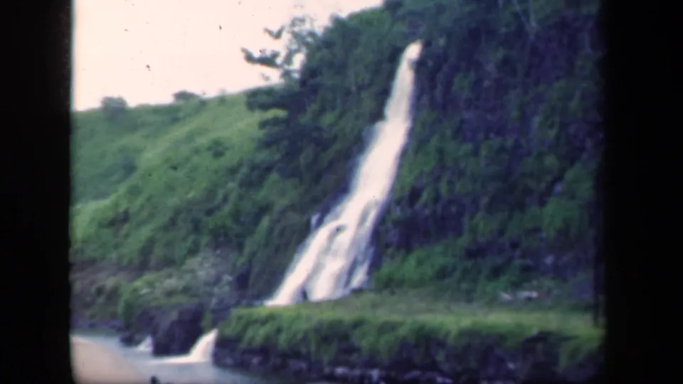 1941 8mm New York home-movie frame showing a waterfall on a lush hillside above a river or lake edge.