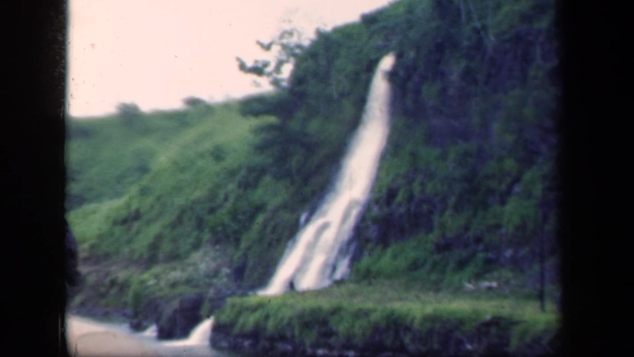 Vintage 8mm frame from New York showing a tall white waterfall cutting through dense green hillside vegetation.