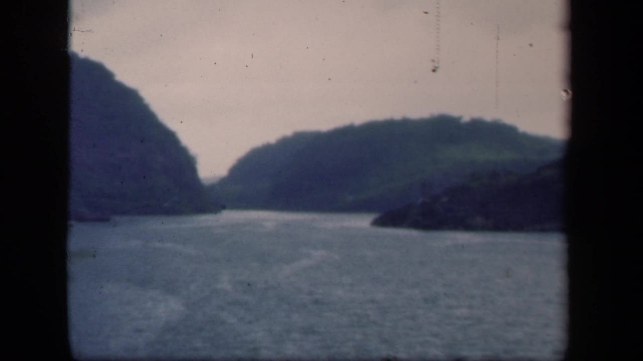 Calm lake water between dark wooded hills under an overcast sky.