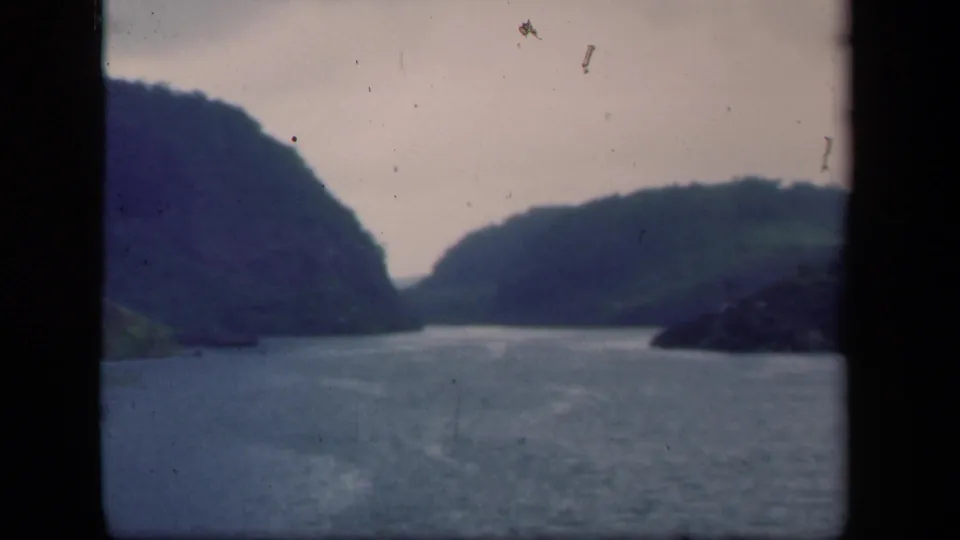 1941 New York 8mm frame of a lake bordered by dark hills, with prominent film scratches and muted color.