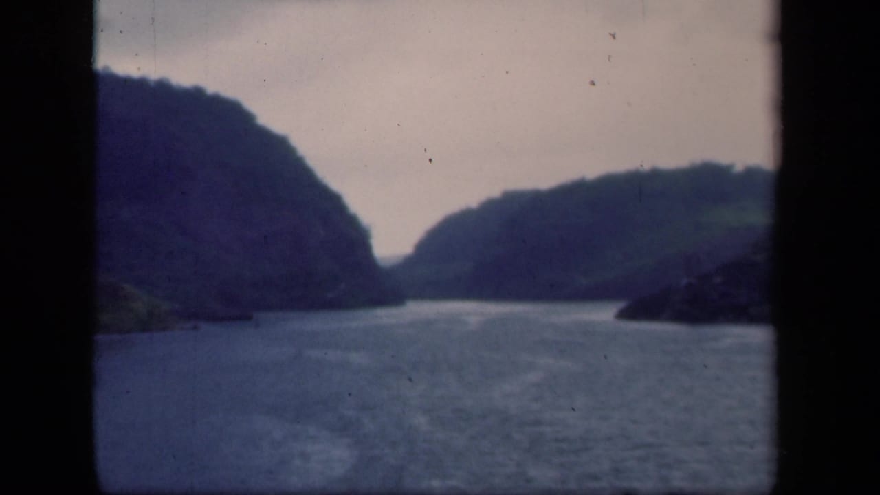 1941 New York home-movie frame showing a bay or river between wooded hills, viewed through dark window-like edges.