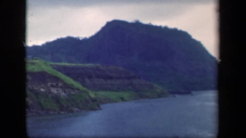 1941 New York 8mm frame with a closer view of green slopes, rocky shoreline, water, and a dark wooded mountain beyond.