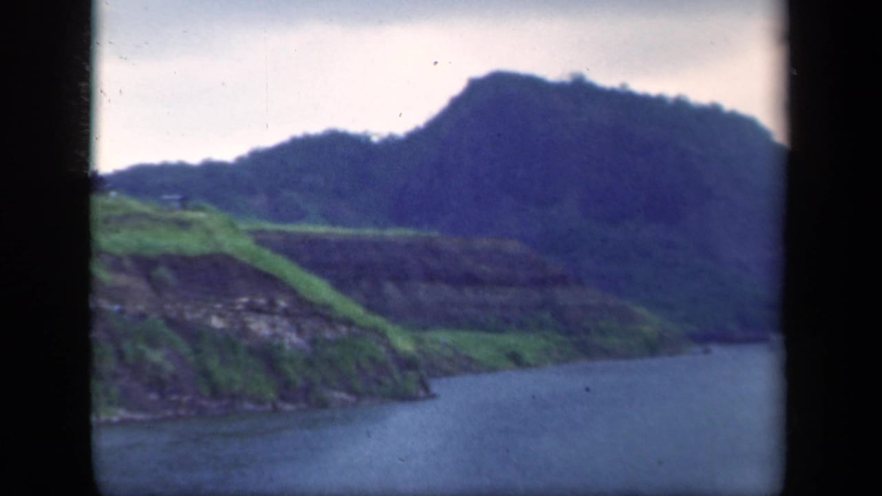 River between green hills under an overcast sky, framed by dark film gate edges.