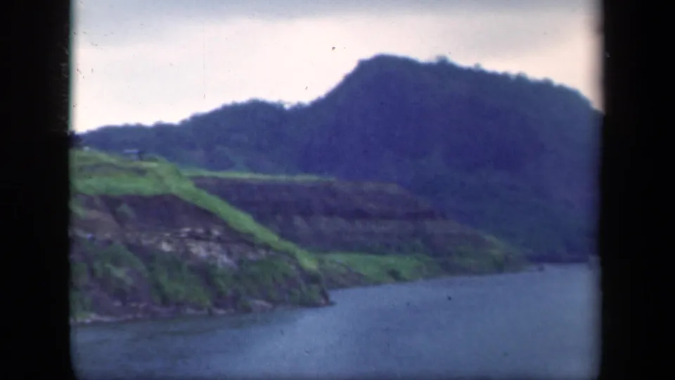 1941 New York 8mm frame showing a calm river below green hills and darker mountain slopes on a cloudy day.