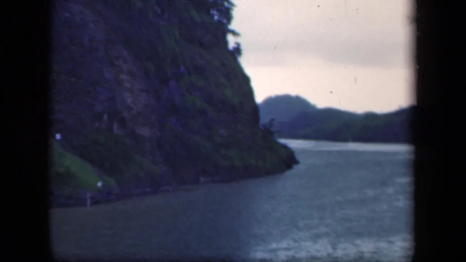 1941 New York home-movie frame showing rippled river water beside a forested slope, with distant hills under a pale sky.